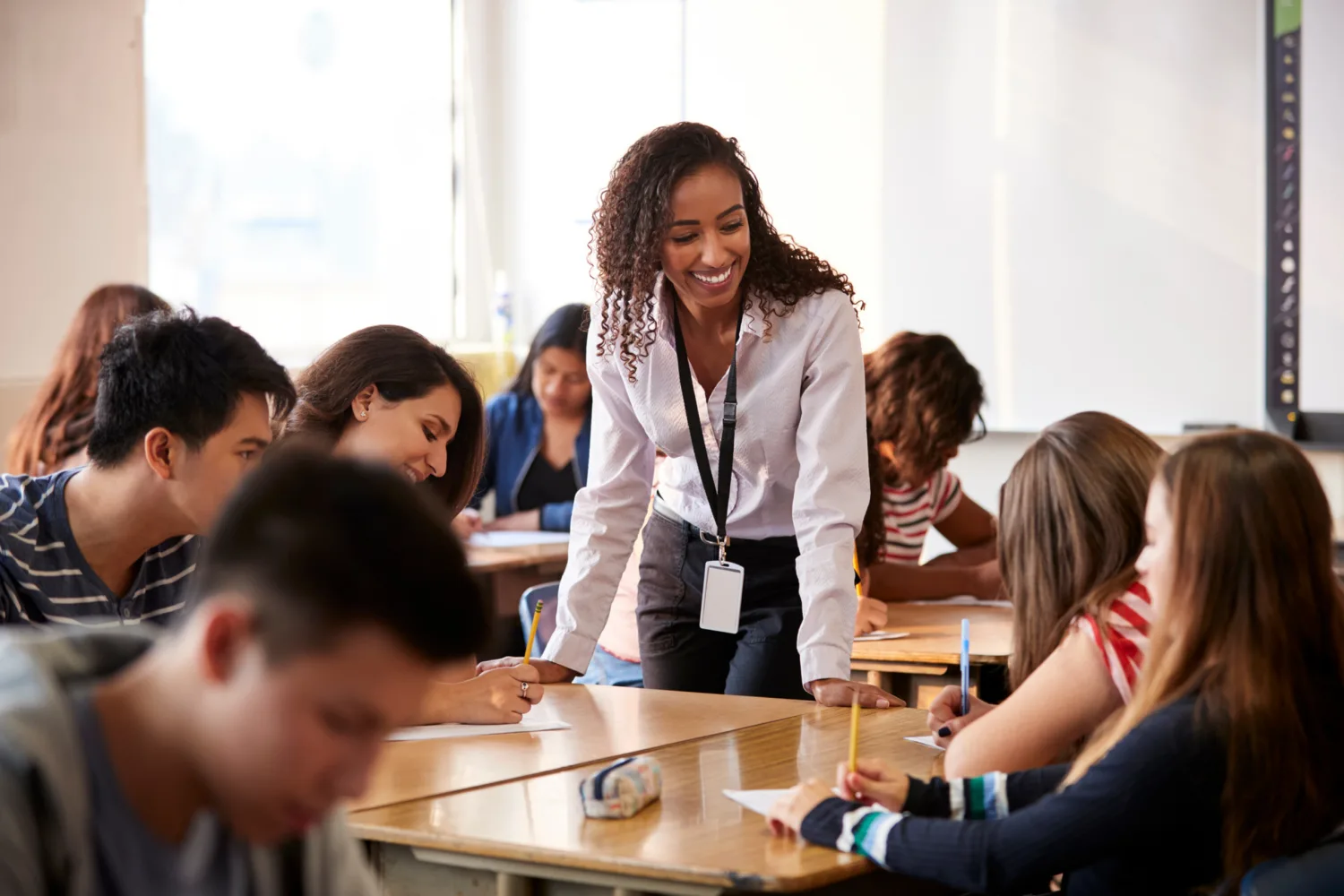 Teacher helping high school students at their desks in a classroom