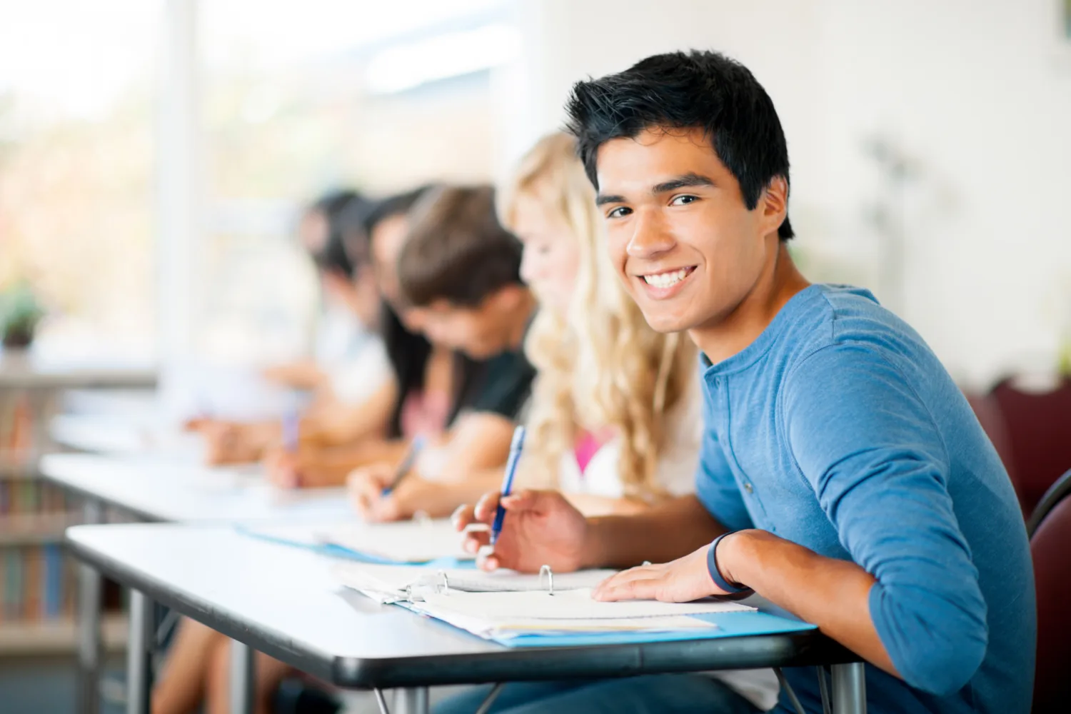 Smiling high school student writing at a classroom desk